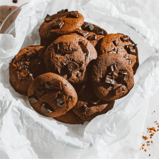 Twelve freshly baked Bakendales standard chocolate chip cookies, stacked and arranged to show their dark-brown color